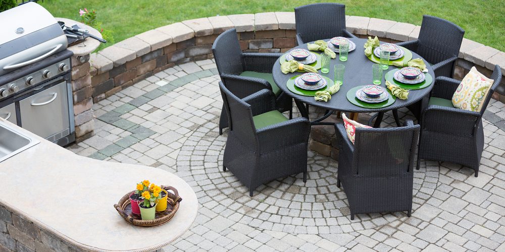 Elegant outdoor living space on a paved brick patio with a summer kitchen and barbecue and a table laid with formal place settings for dinner, high angle view